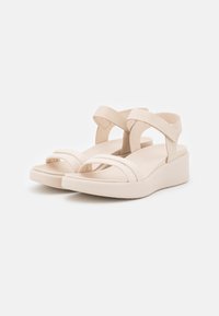 Beige platform sandale s dizajnom križnog remenčića, izrađene od glatkog materijala. Imaju široku podlogu za stopala i teksturiranu potplatu za bolje prianjanje.