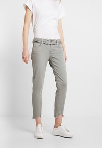 Ljusgråa cropped jeans med fransad nederkant, featuring ett midjeband med bältesöglor och framfickor. Matchas med vita sneakers.