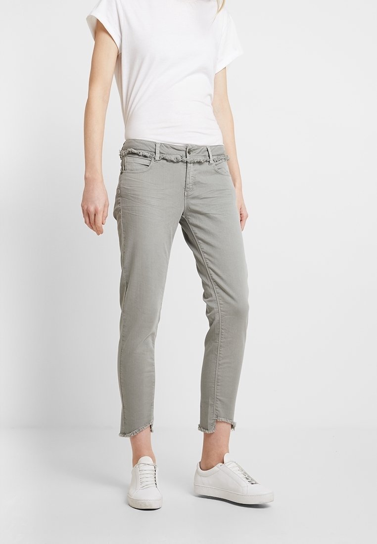 Ljusgråa cropped jeans med fransad nederkant, featuring ett midjeband med bältesöglor och framfickor. Matchas med vita sneakers.