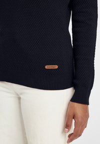 Marineblauer Pullover aus strukturiertem Stoff mit geripptem Saum und Bündchen. Verfügt über ein braunes Leder-Logoschild an der unteren Seite.