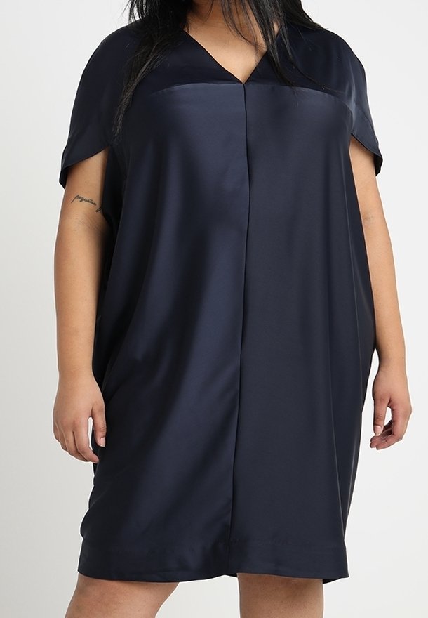 Femme portant une robe ample, à manches courtes, bleu foncé, avec un col en V et une couture verticale au centre devant.