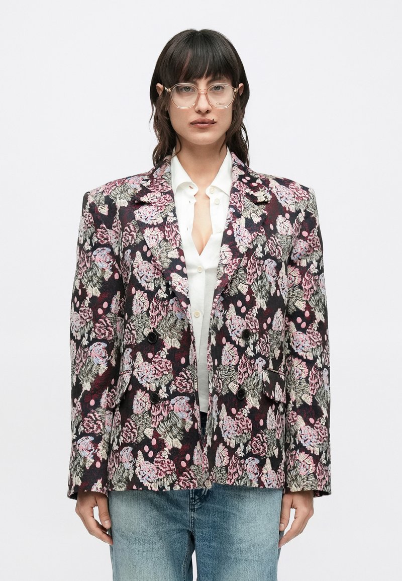 Σακάκι με λουλουδάτο σχέδιο σε σκο ύρες αποχρώσεις με ροζ, μωβ και πράσινες λεπτομέρειες. Δομημένη σιλουέτα, αιχμηλές πέτες και διπλό μπροστινό μέρος.