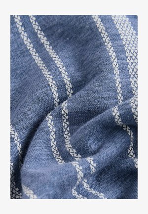 Blått tyg med en strukturerad väv, med vita diagonala ränder och intrikata mönster. Mjukt, fallande material med synlig djup.