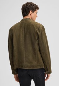 Olijfgroene suede jas met een gladde textuur, een getailleerde pasvorm en een minimalistisch ontwerp. Beschikbaar met een kraag en knoopdetails.