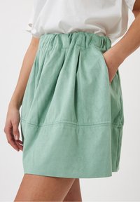 Ljusgrön, mjuk kjol i tyg med veck, elastisk midja och sidofickor; har en slät textur och enkel linjesöm.