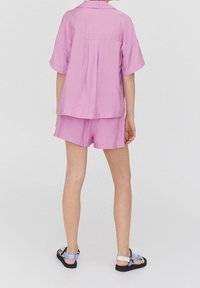 Camisa rosa de manga corta y pantalones cortos a juego, con un corte holgado y tejido texturizado. Sandalias negras con tiras multicolores completan el look.