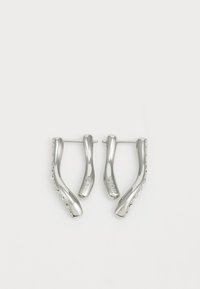 Pendientes de aro de plata con un diseño ondulado, que presentan una superficie lisa y el nombre de la marca grabado en el borde exterior.