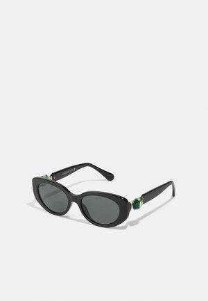 Ochelari de soare negri, de tip cat-eye, cu lentile întunecate. Au accente aurii și verzi pe temple. Rame din plastic neted și design elegant.