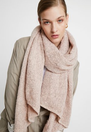 Écharpe texturée rose clair en matériau doux, drapée autour du cou, avec des bords bruts et une apparence chaleureuse et accueillante.