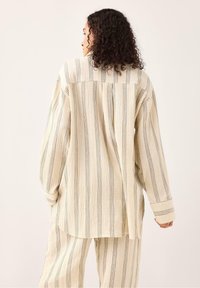 Cremefarvet stribet oversized skjorte med lange ærmer, der har skiftende mørke og lyse vandrette striber samt en plissé bagpå.