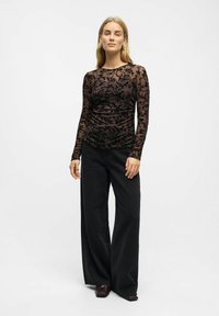 Permatomas juodas ilgomis rankovėmis marškinėliai su gėlių raštu, derinami su plačiomis juodomis džinsomis. Sklandi tekstūra, prigludusi siluetas ir apvalus iškirptė.