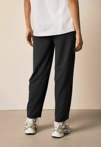 Czarne spodnie dresowe wykonane z miękkiej tkaniny, o luźnym kroju, z bocznymi kieszeniami i ściągaczami na nogawkach. W zestawieniu z szarymi trampkami.