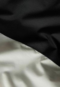 Tkanina tekstylna z czarną, teksturowaną powierzchnią z jednej strony i gładką, jasnoszara powierzchnią z drugiej, z widocznym czystym szwem.