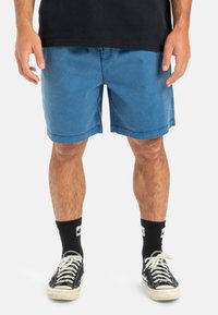 Șorturi din denim albastru cu buzunare laterale, un croi lejer și o margine dreaptă. Asortate cu șosete negre și adidași clasic negri.