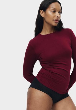 Blusa de manga larga en burdeos, hecha de una tela suave y elástica, combinada con pantalones negros. Presenta un escote redondo y un diseño ajustado.