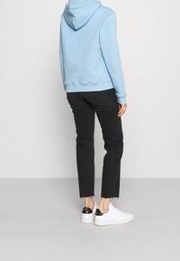 Sudadera con capucha azul claro, vaqueros negros de corte ajustado y zapatillas blancas con detalles en negro. Los vaqueros tienen el dobladillo deshilachado.