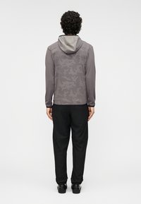 Γκρι μπουφάν με κουκούλα και διακριτικό σχέδιο υφής, συνδυασμένο με μαύρο παντελόνι και παπούτσια. Η εικόνα δείχνει καθαρά την πλάτη της ενδυμασίας.