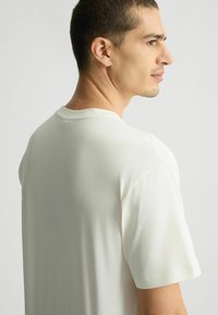 T-shirt beige chiaro realizzato in morbido cotone, dotato di maniche corte, scollatura rotonda e una vestibilità rilassata con dettagli minimi.