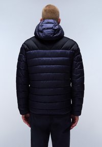 Marineblauwe pufferjack met een capuchon, voorzien van diagonale stiksels op het bovenste gedeelte en horizontale quilting. Gladde textuur en verstelbare capuchon.