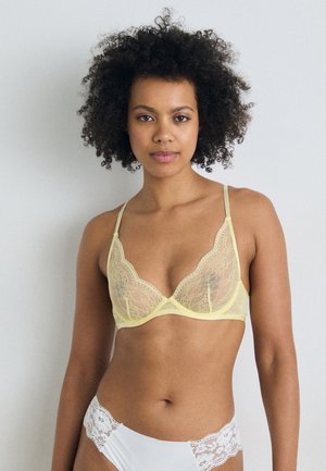 Brassière en dentelle de couleur jaune doux avec des bords festonnés et des bretelles fines réglables, associée à une culotte blanche ornée de dentelle.