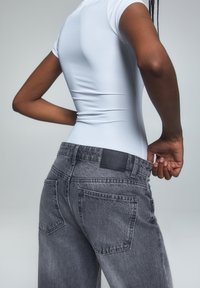 Kapealinen valkoinen bodysuit yhdistettynä korkeavyötäröisiin, haalistuneisiin harmaisiin denim-farkkuihin, joissa on takataskut ja musta nahkaiset tarrat vyötäröllä.