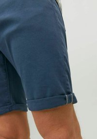 Pantaloni corti in cotone blu navy con orli risvoltati, caratterizzati da una trama liscia e da sottili dettagli di cucitura. Inquadratura ravvicinata del lato.