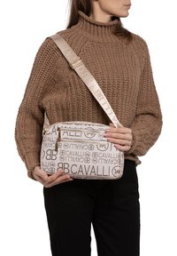Borsa a tracolla beige con logo in rilievo, chiusura con zip e tracolla regolabile. Realizzata in materiale testurizzato con un accento liscio.