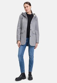 Grau melierter Wollmix-Mantel mit Kapuze, ausgestattet mit vier Knöpfen, Klappentaschen und kontrastierendem Innenfutter. Trägt man mit blauen Jeans und schwarzen Stiefeln.