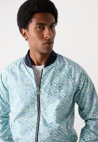 Leichte, gemusterte Bomberjacke in Aqua- und Grüntönen. Mit einem Reißverschluss vorne und einem navyfarbenen Kragen; geometrisches Design über die gesamte Jacke.