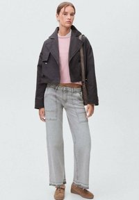 Giacca cropped nera, top rosa, jeans larghi grigi con tasche cargo, scarpe marroni. Outfit casual con textures e colori misti.
