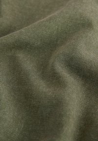 Primo piano di un tessuto verde oliva rugoso che mostra una finitura a coste sottili e pieghe morbide.