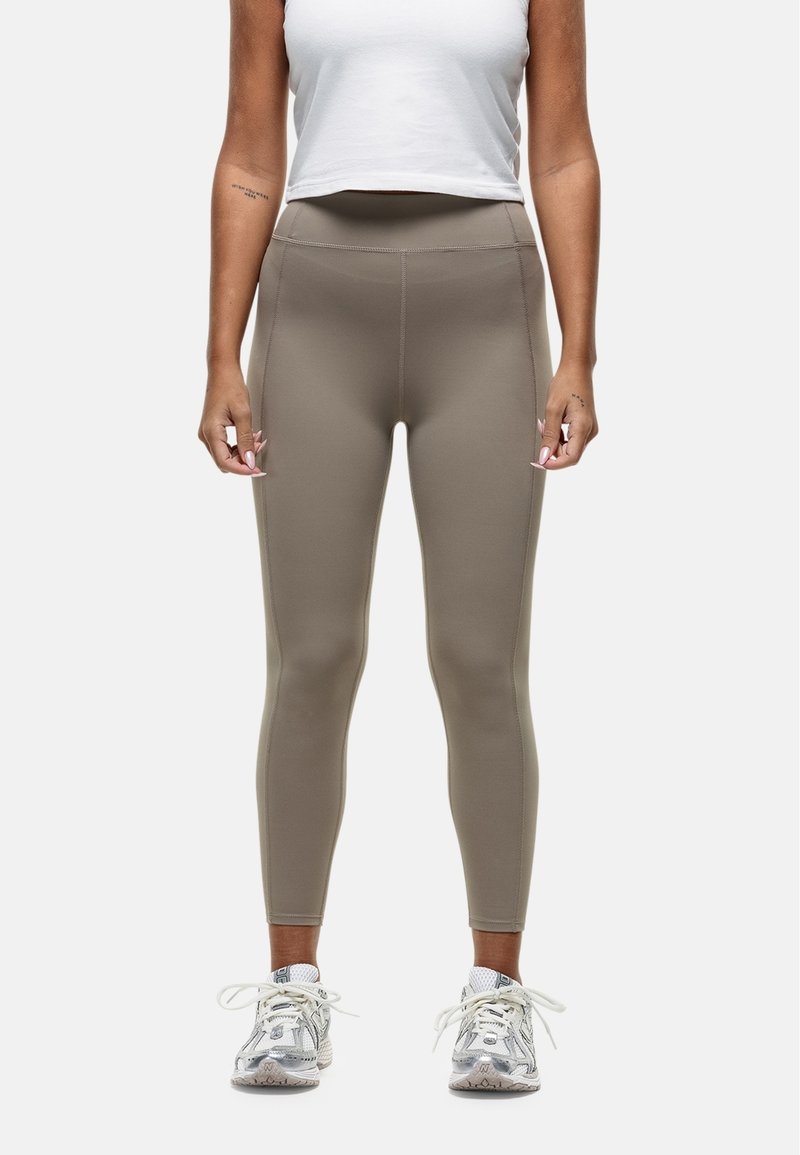 Leggings in een gedempt taupe-kleur, slim-fit ontwerp, hoge tailleband, gladde textuur, met subtiele zijnaad en gecombineerd met witte sneakers.