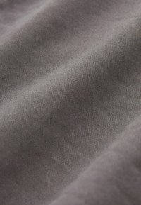 Harmaa kangas, jossa on hieno pinta ja hienovarainen kiilto, sisältäen vinon kudontamallin. Materiaali näyttää pehmeältä ja sileältä.