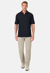 La camiseta polo negra presenta mangas cortas y un collar puntiagudo, combinada con pantalones beiges y zapatillas deportivas de color claro. Diseño sencillo, sin patrones.