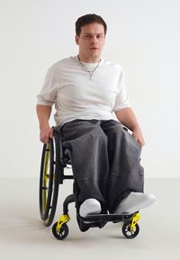 Crni invalidska kolica s žutim detaljima, s velikim crnim kotačima. Nosim bijelu majicu i sive široke hlače, s bijelim tenisicama.