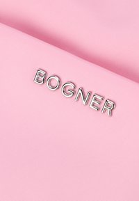 Ružová textúrovaná tkanina s vyšívaným strieborným logom "BOGNER" naprieč povrchom, ktorá ukazuje čisté línie a hladký povrch.