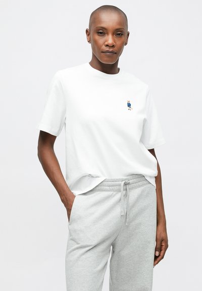 Λευκό βαμβακερό T-shirt με ένα μικρό κεντημένο χαρακτήρα, συνδυασμένο με ανοιχτό γκρι παντελόνι φόρμας. Απλός σχεδιασμός, χαλαρή εφαρμογή και στρογγυλή λαιμόκοψη.