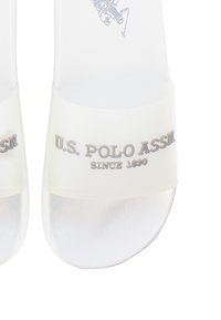 Chanclas blancas y translúcidas con una textura suave y una tira ancha que presenta el texto en relieve "U.S. POLO ASSN SINCE 1890."
