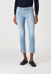 Világoskék, bokáig érő, slim fit farmernadrág, oldalsó cipzárokkal a száraknál és öt zsebes designnal, elülső gombos zárással.