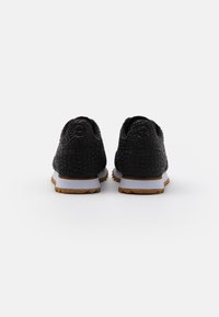Black textured sneakers with a reptile-like pattern, white midsole, and brown rubber outsole. Rounded toe and padded collar.