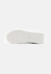 Hvit gummisåle til sneakers med et strukturelt mønster, og "HUGO" preget i en kontrastfarge på siden.