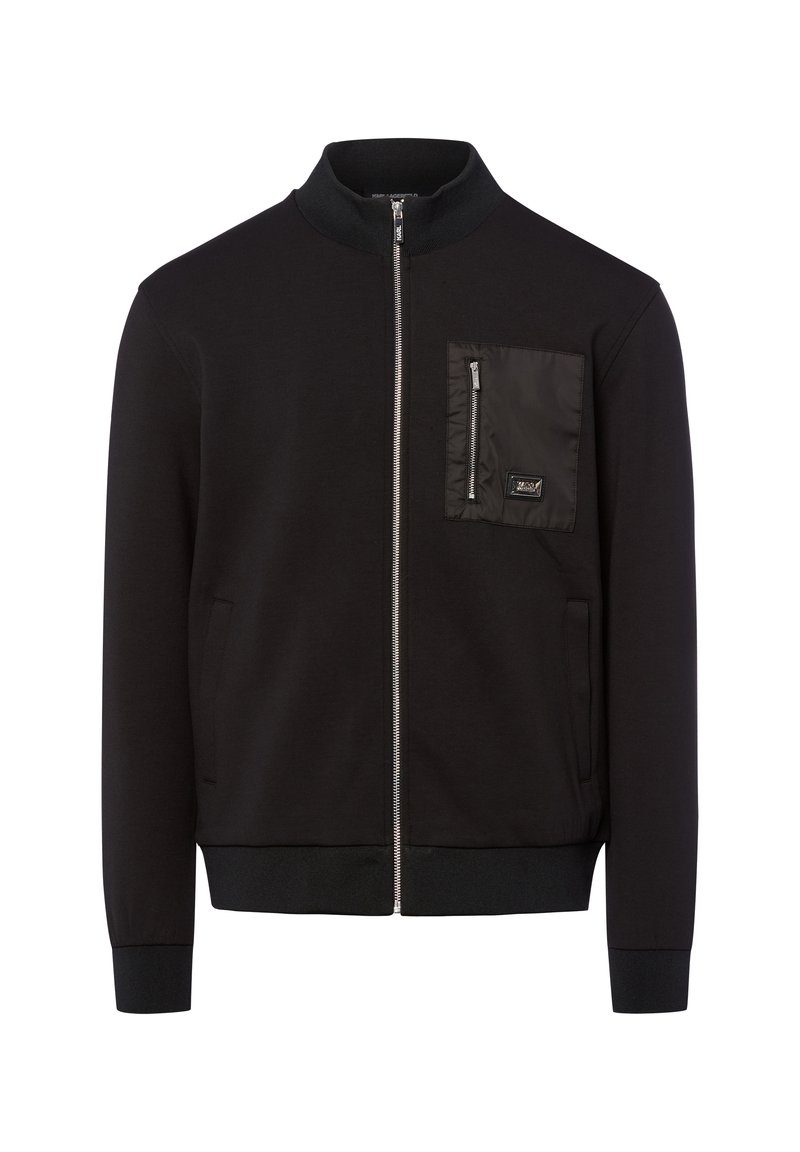 Zwarte zip-up jas met geribde kraag, manchetten en zoom, voorzien van een ritszak op de borst met een klein logo-patch.