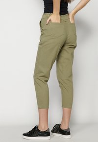 Pantalones caqui con cintura elástica y dos bolsillos traseros. Longitud recortada y tejido de algodón suave, combinados con zapatillas negras.