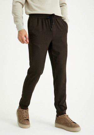 Braun karierte Jogginghosen mit elastischem Bund und Kordelzug, kombiniert mit hellbraunen Sneakers. Sanfter, lässiger Stoff.