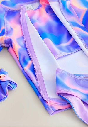 Dětská plavková souprava v pastelově modré, fialové a růžové barvě s tie-dye vzorem, položená na plocho, která ukazuje švy a texturu látky.