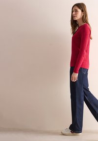 Rotes Langarmoberteil mit Rundhalsauschnitt, kombiniert mit weiten, dunklen Jeans und weißen Sneakers. Einfaches Design, lässige Passform.