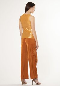 Top sin mangas de color naranja brillante con una textura brillante, combinado con pantalones de pierna ancha que cuentan con bolsillos laterales tipo cargo y un acabado suave.