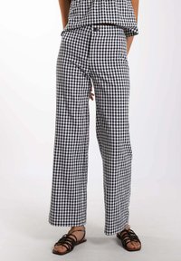 Pantalones de pierna ancha de cuadro vichy en blanco y negro con una cintura alta, confeccionados en una tela ligera, complementados con sandalias planas.