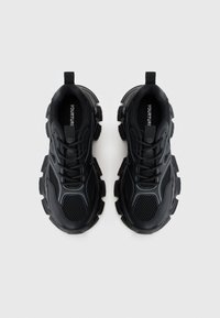 Black athletic shoes with a mesh upper, thick rubber soles, and prominent contouring. Features textured detailing and reinforced toe area.