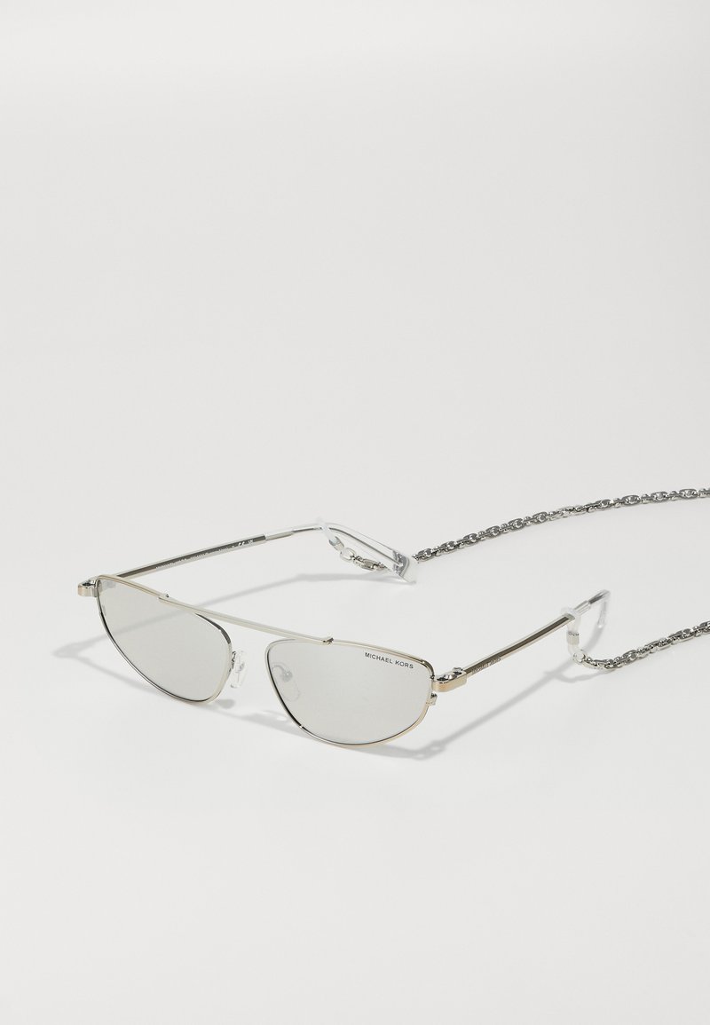 Occhiali da sole in metallo argentato con forma a occhio di gatto, lenti trasparenti e un'attaccatura decorativa in catena argentata per una vestibilità sicura. Etichetta: Michael Kors.